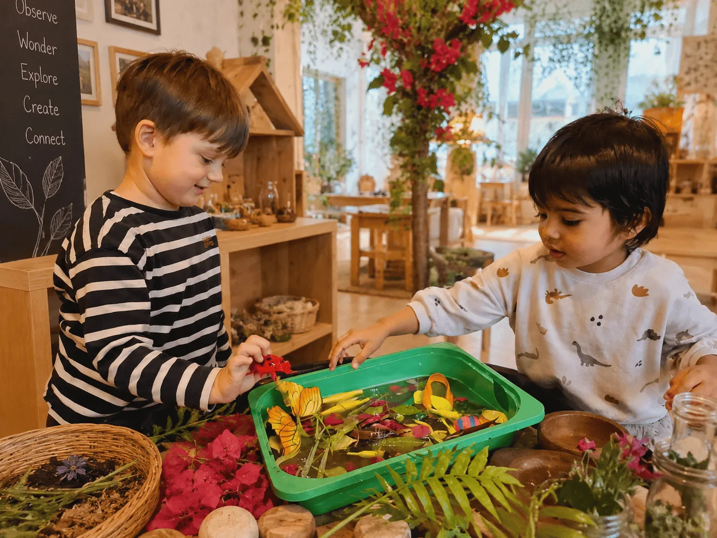 Two children exploring leaves and natural materials in a tray