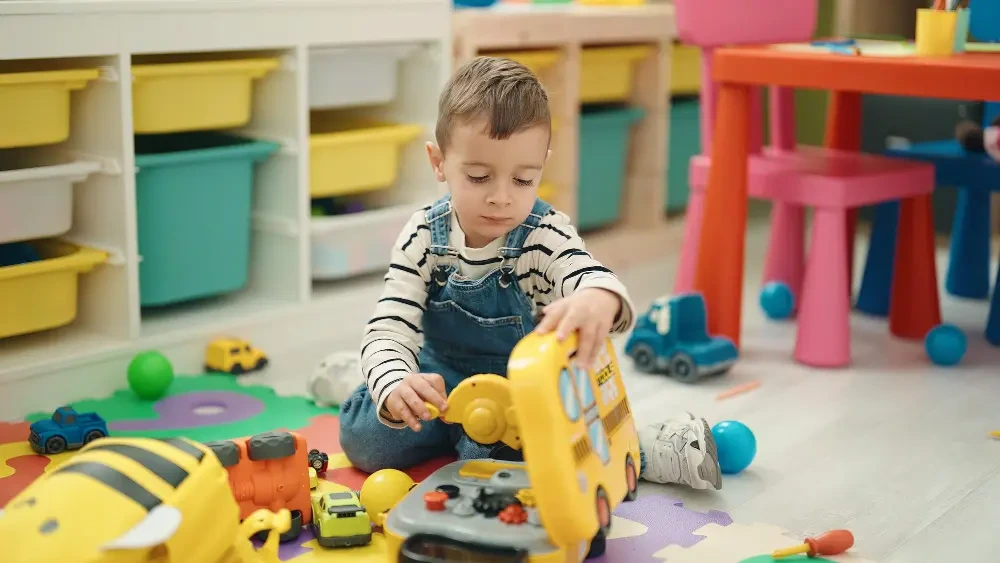 Toddler playing with toy vehicles on a playroom floor